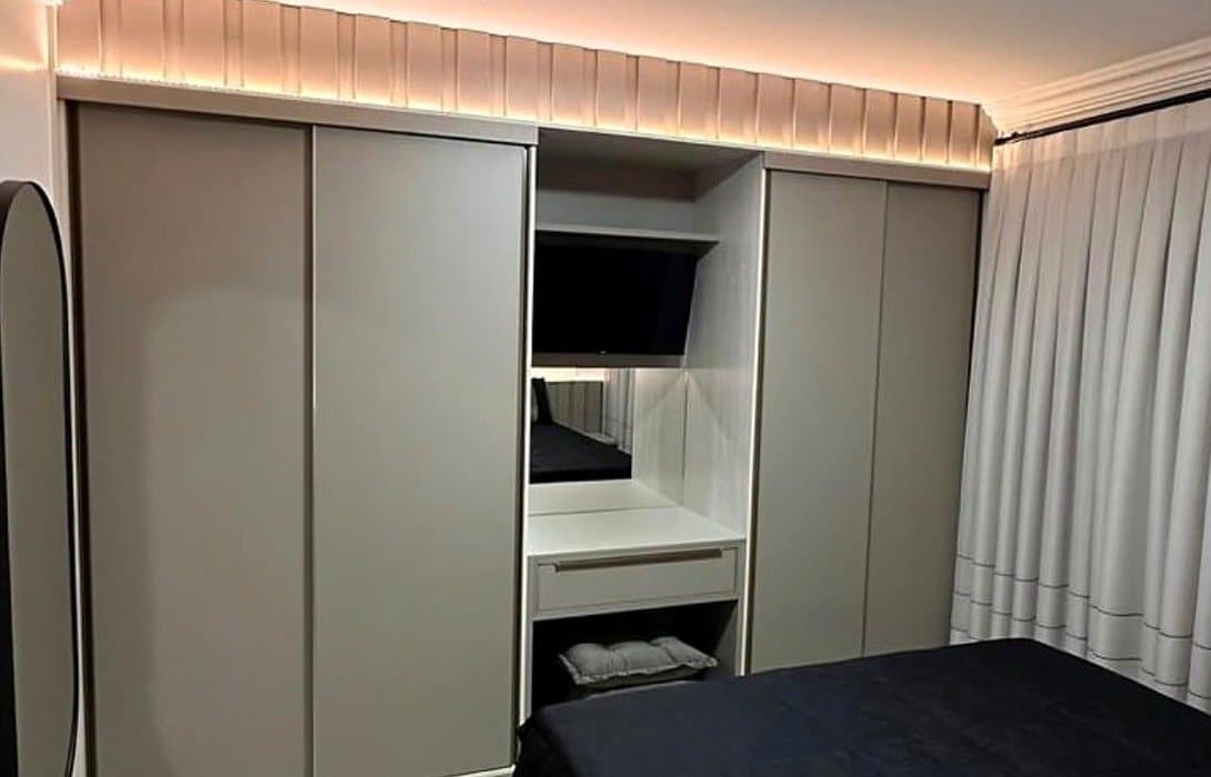 Guarda-roupa cinza claro com nicho central para TV e penteadeira, e acabamento ripado iluminado no topo
